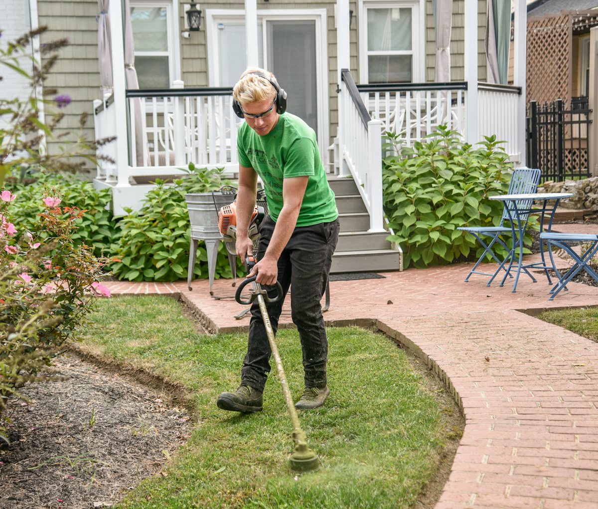 A landscaper edging a lawn beside a home with a string trimmer