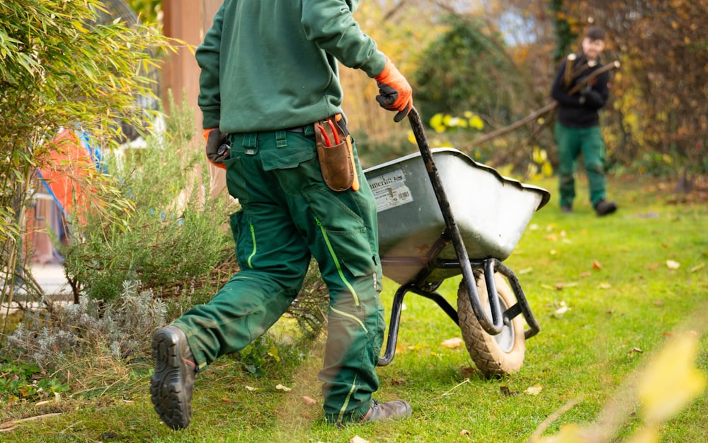 A groundskeeper clearing garden waste into a wheelbarrow